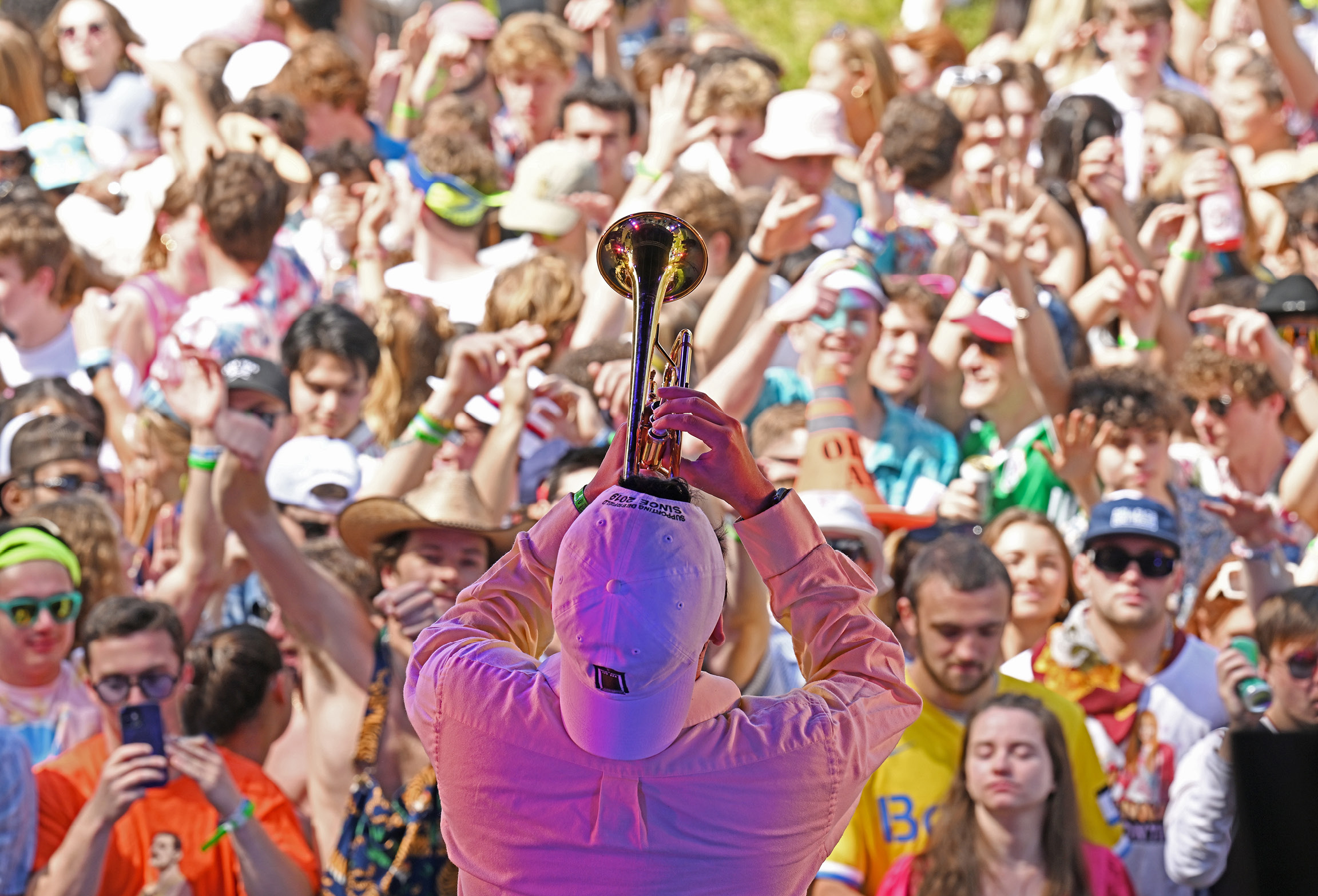 A musician blows a trumpet at Floralia in front of a crowd.