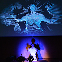 Photo of a performance with a figure being projected onto a screen