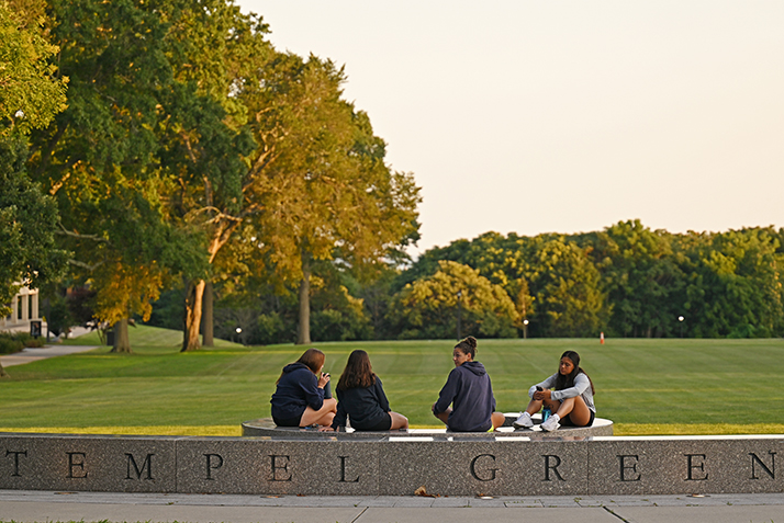 Students relax on the Tempel Green sign as the sun begins to set on Arrival Day.