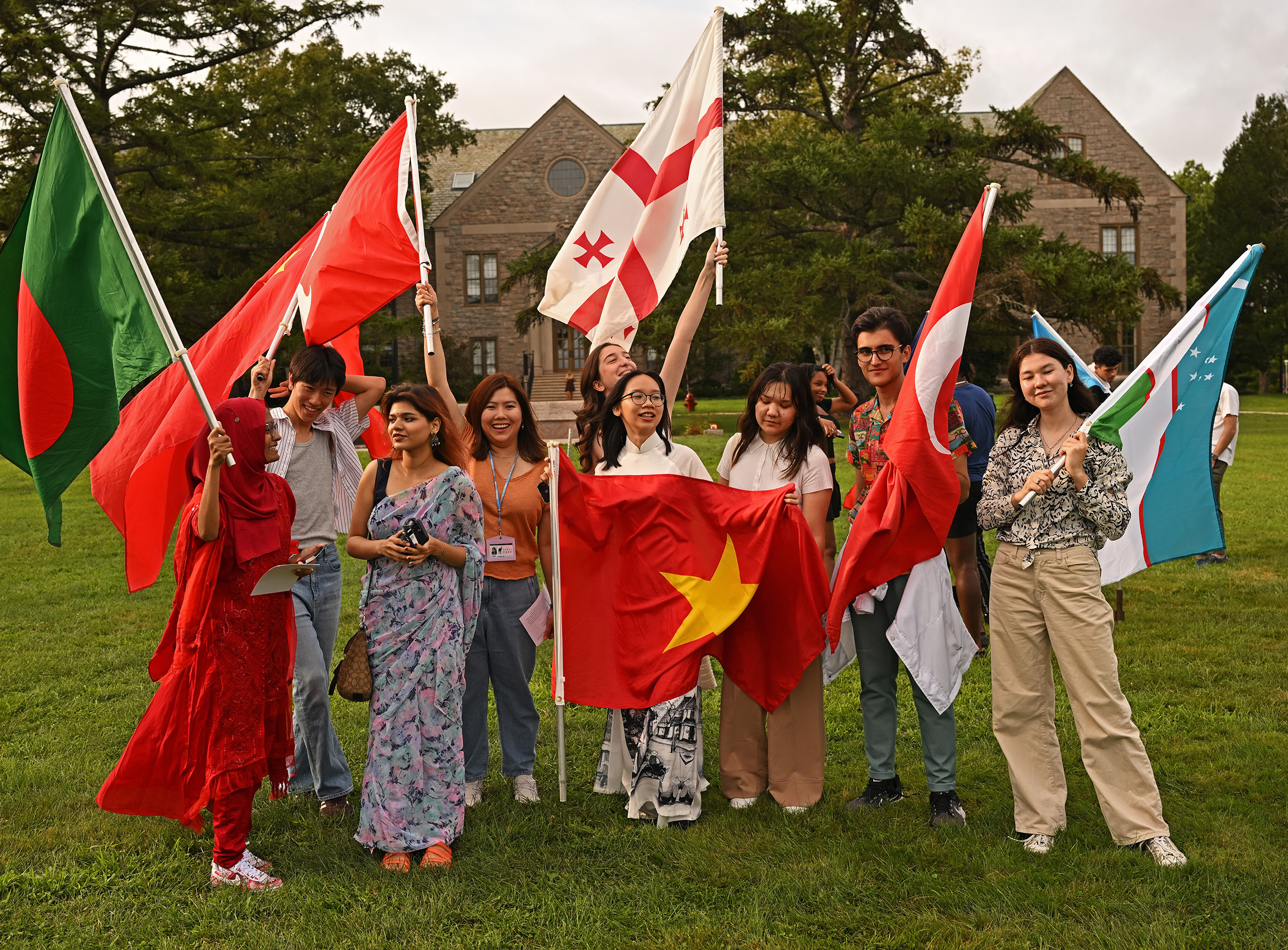 A group of international students stands in front of the flags at Convocation.
