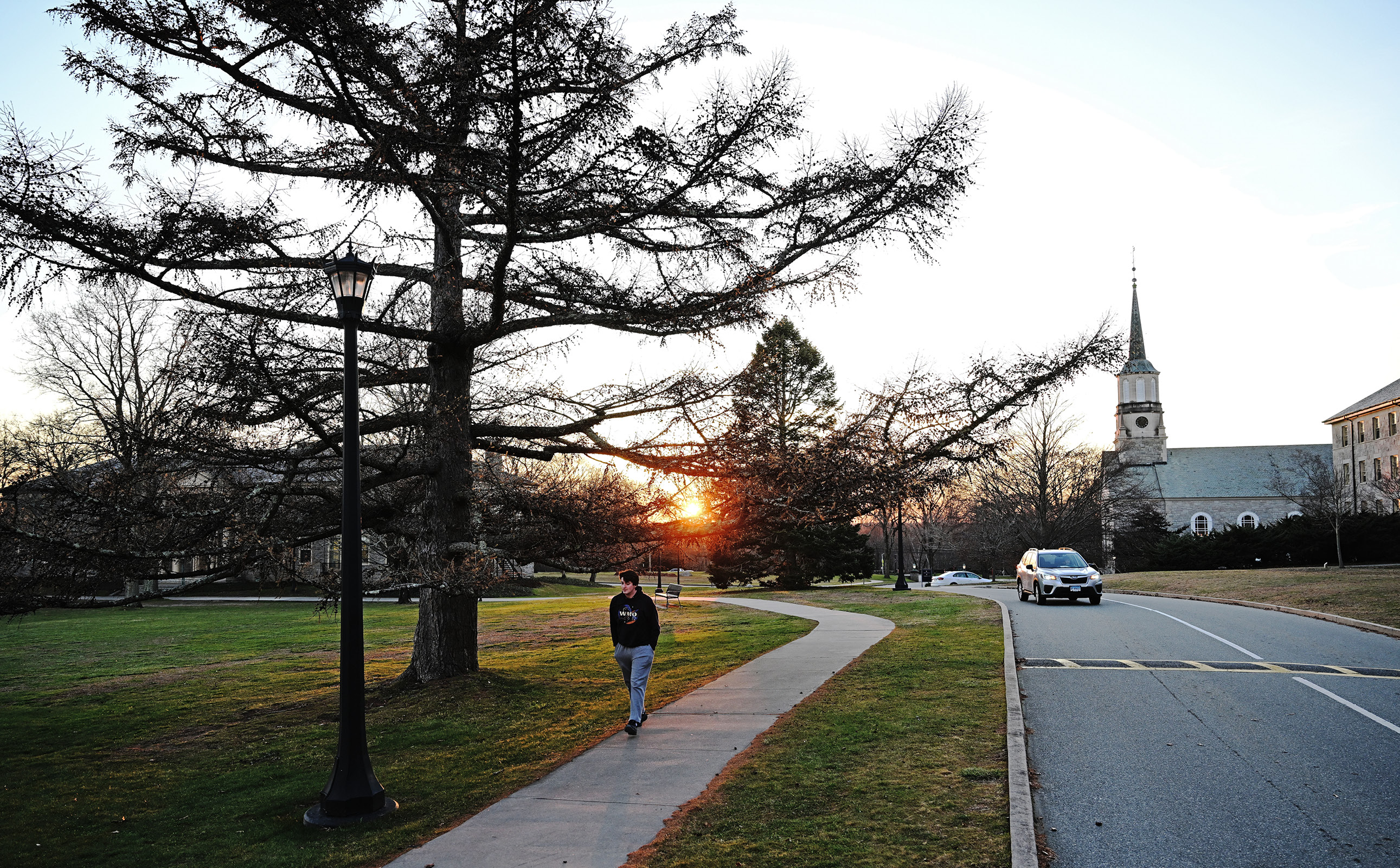 Student walks over Chapel Way with a sunset in the background.