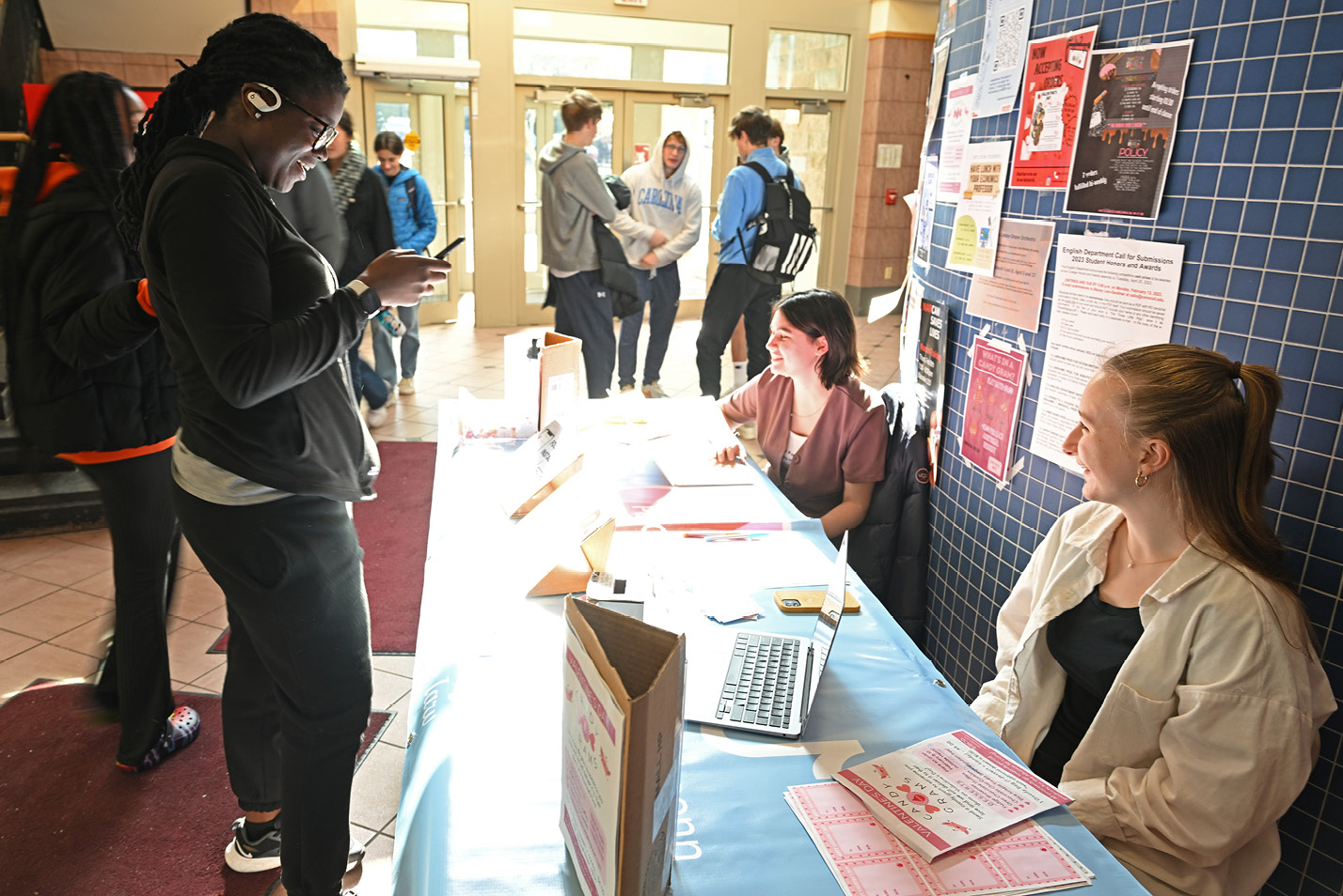 Anike Abegunde ’24 purchases a Candygram from Period. club officers Norah Morrissey ’25, left, and Lydia Evans ’25 at their table set up in the Harris Dining atrium.