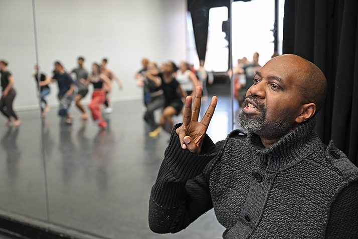 choreographer gives instructions to dancers reflected in studio mirror