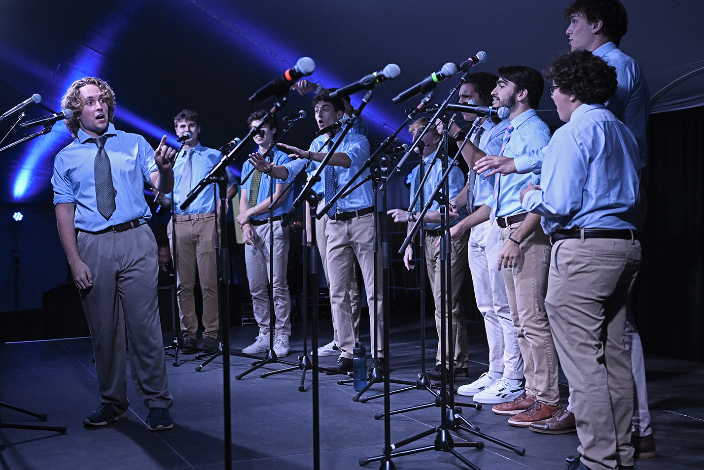 An all-male a cappella group in shirts and ties performs on stage.