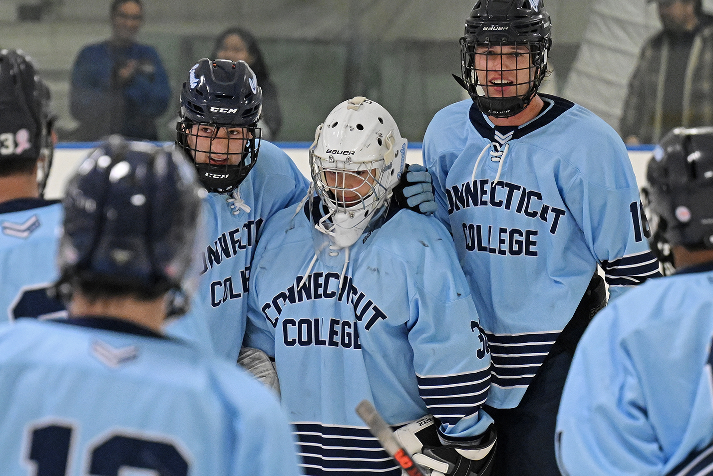 Hockey players gather around their goalie to congratulate him for a winning game.