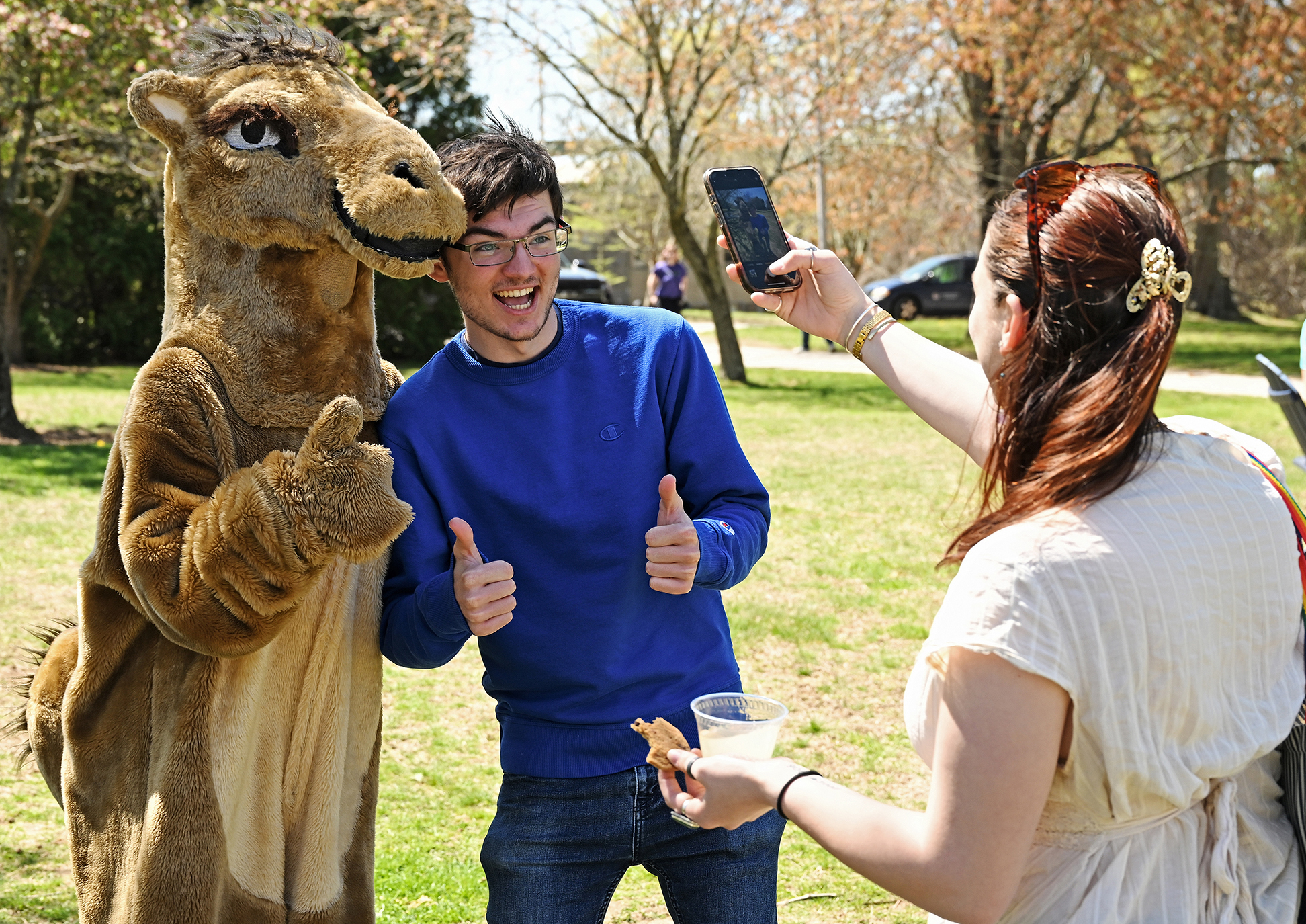 A student gives two thumbs-up as he poses for a photo with a camel mascot.