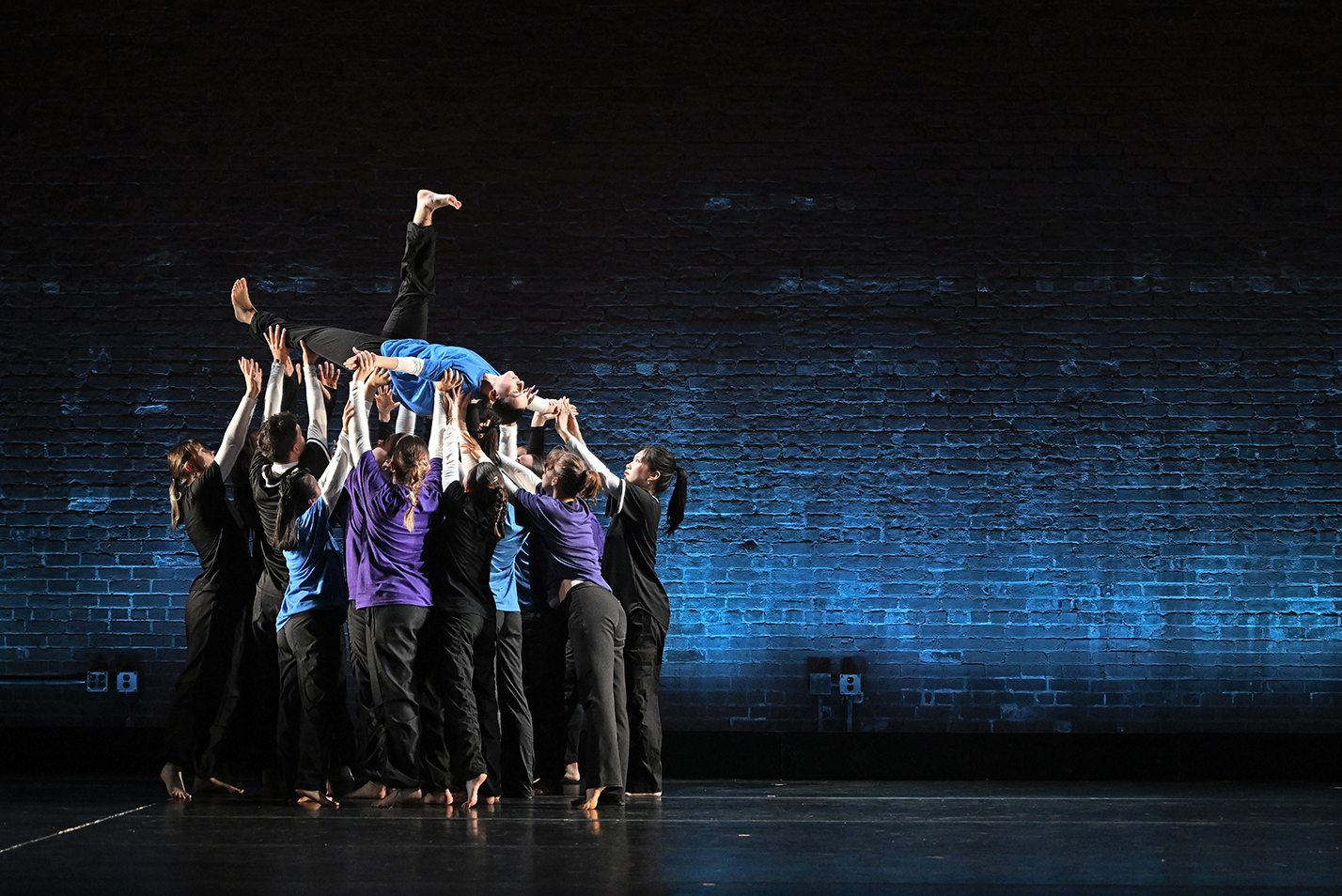 A lone dancer is lifted off stage by a group of dancers during a performance.