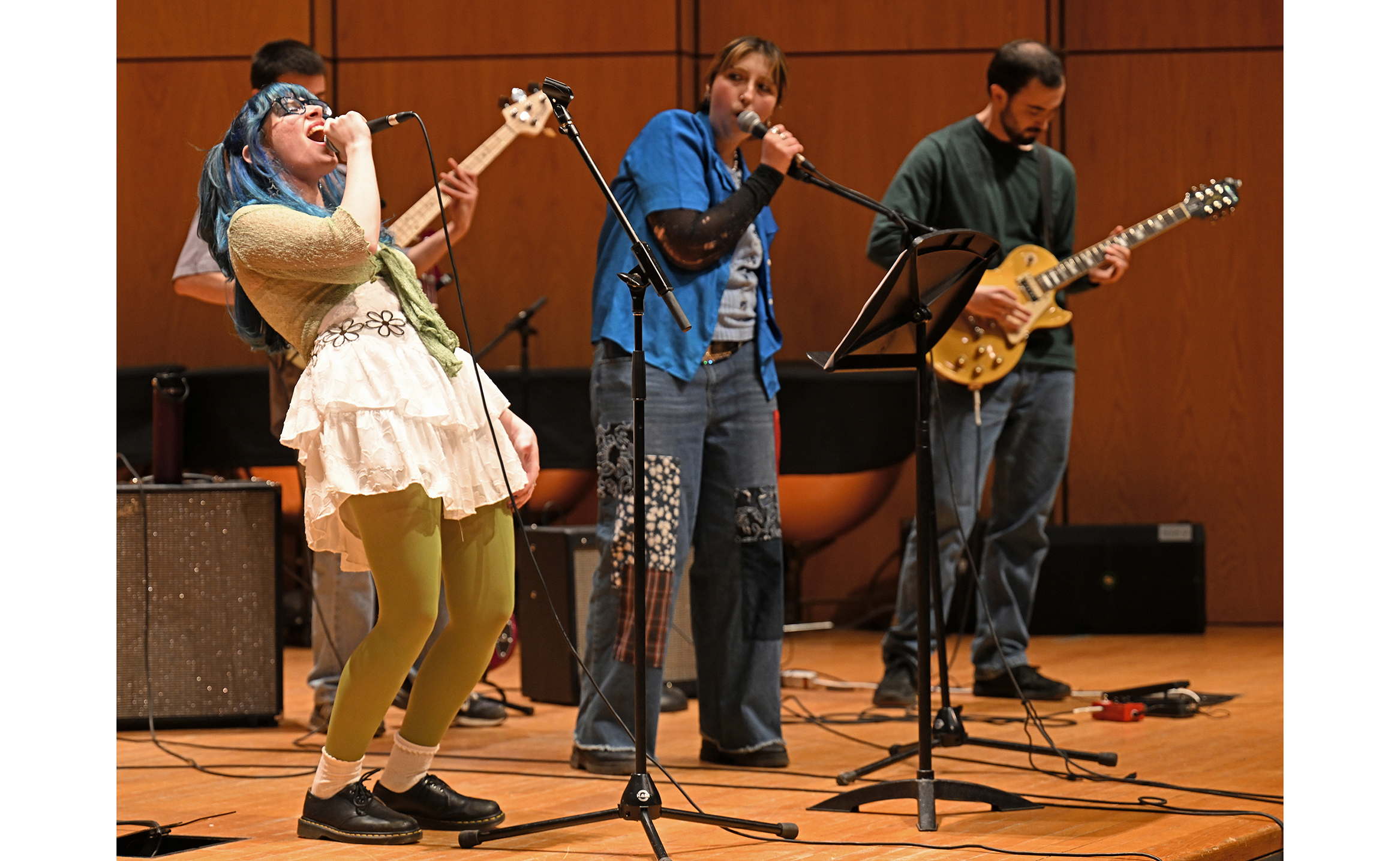 A student in a skirt belts out a rock song during a recital in a concert hall.