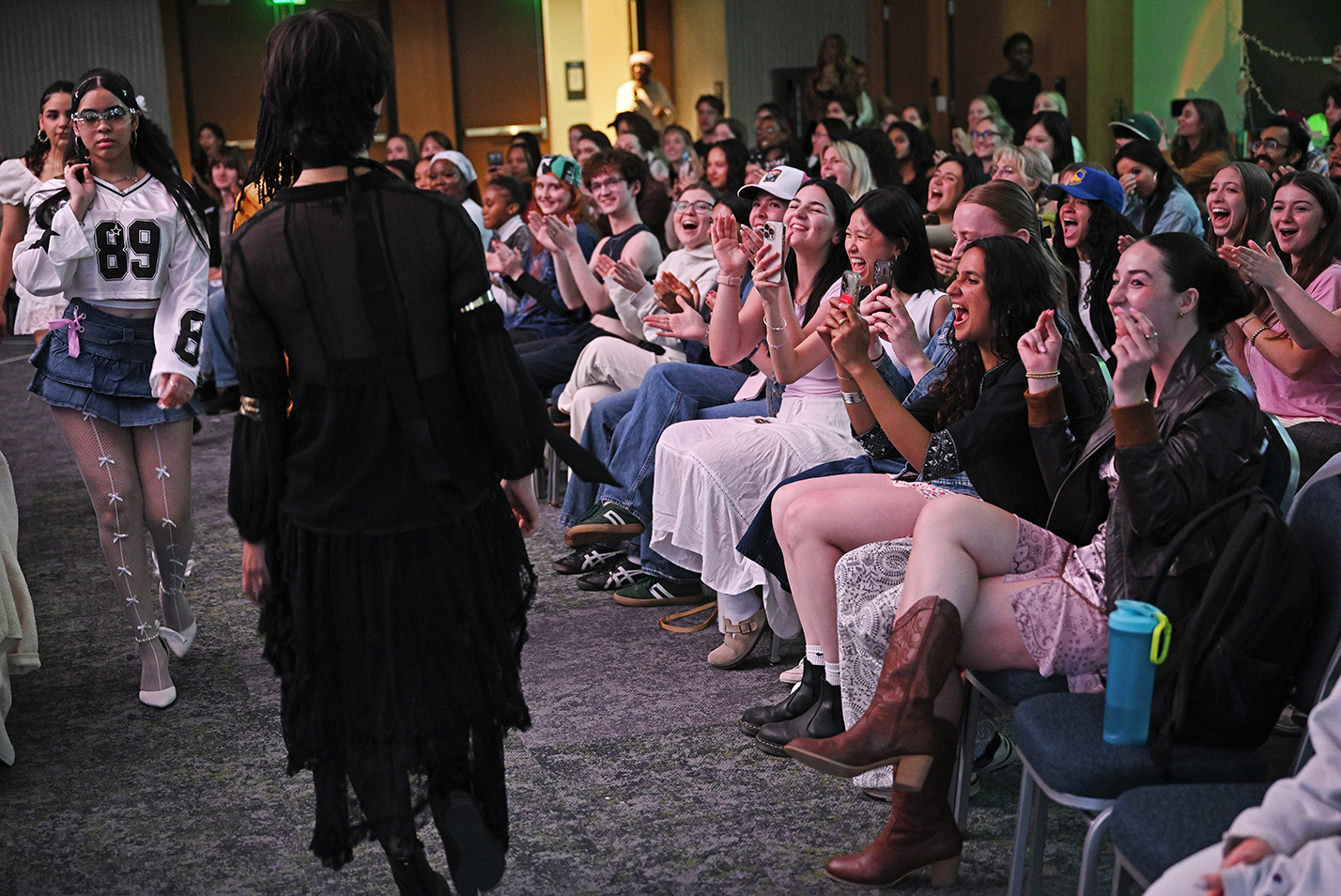 The audience cheers on students performing in a fashion show.
