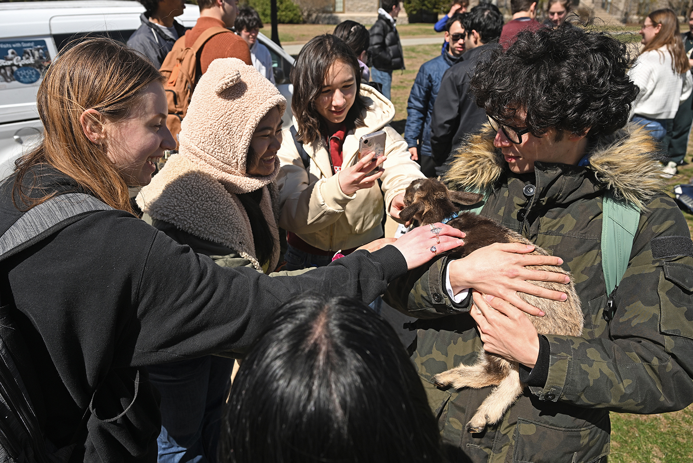 Students gather around to pet a baby goat being held by a classmate.