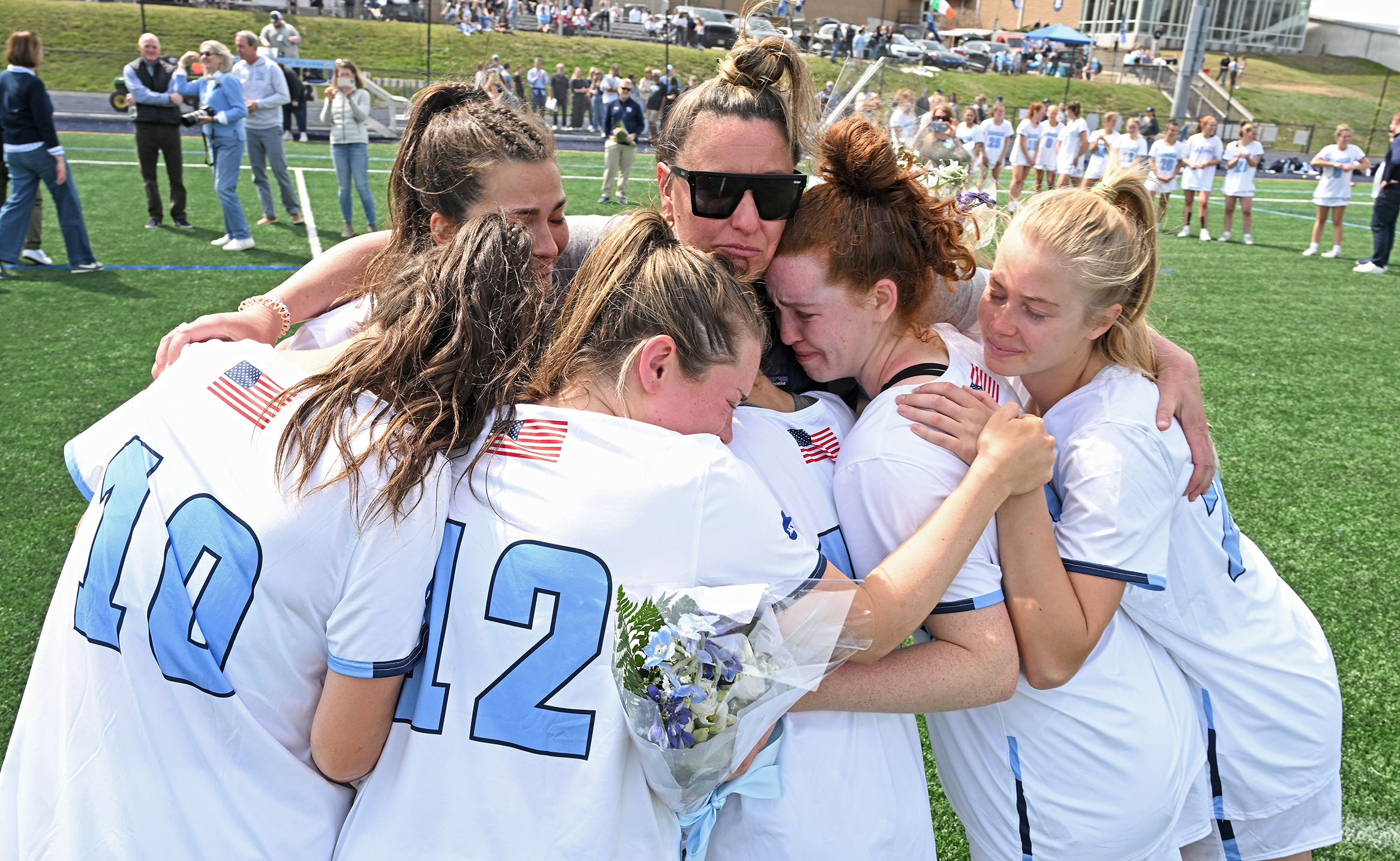 Five women's lacrosse players gather around their coach for a group hug on their Senior Day.