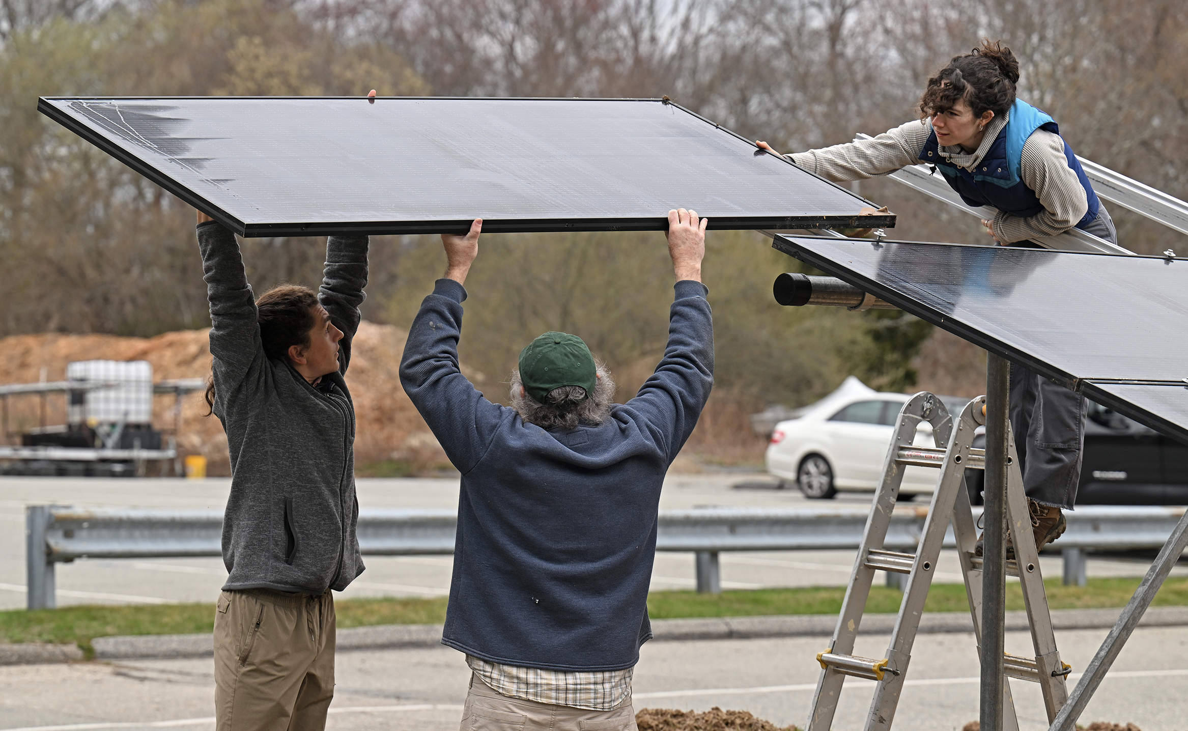 Three people lift a solar panel into place.