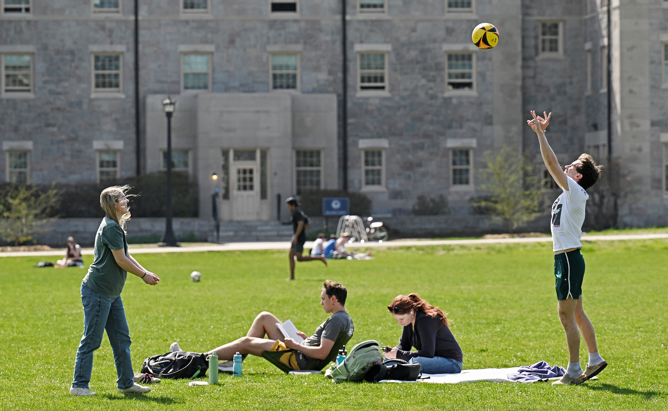 Students bounce a volleyball around while enjoying a warm, sunny, spring day on the college green.