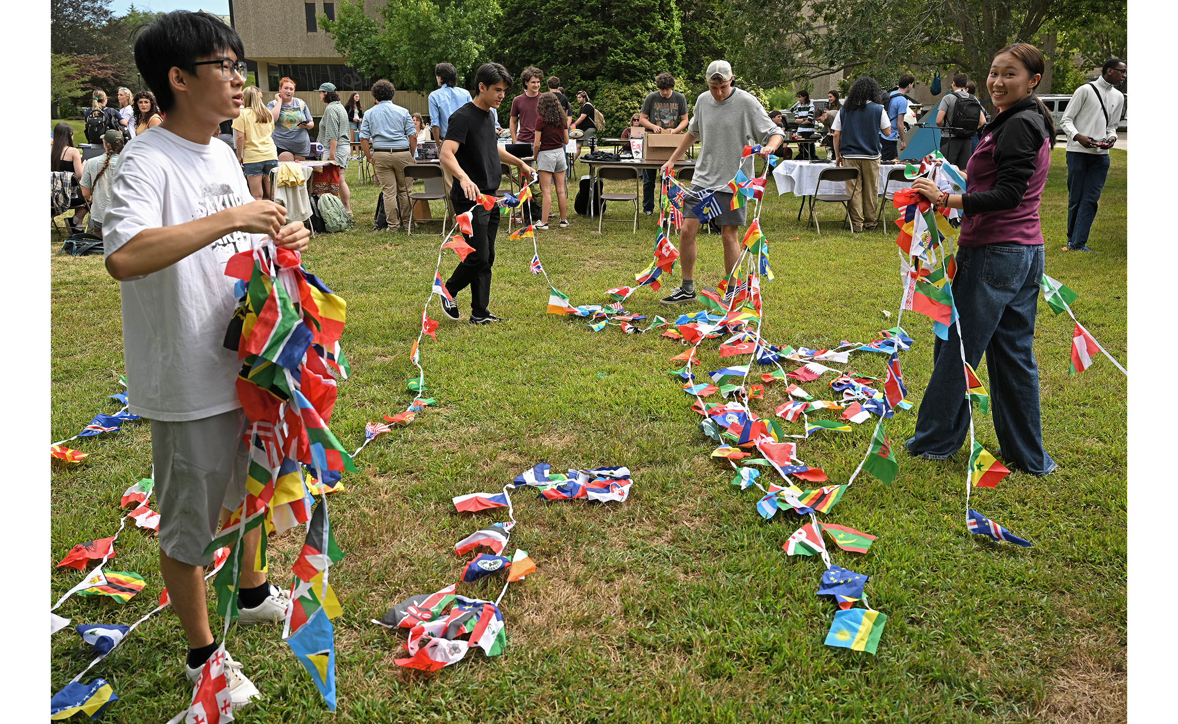 A group of students work to untangle a string of international flags standing in a grassy field.