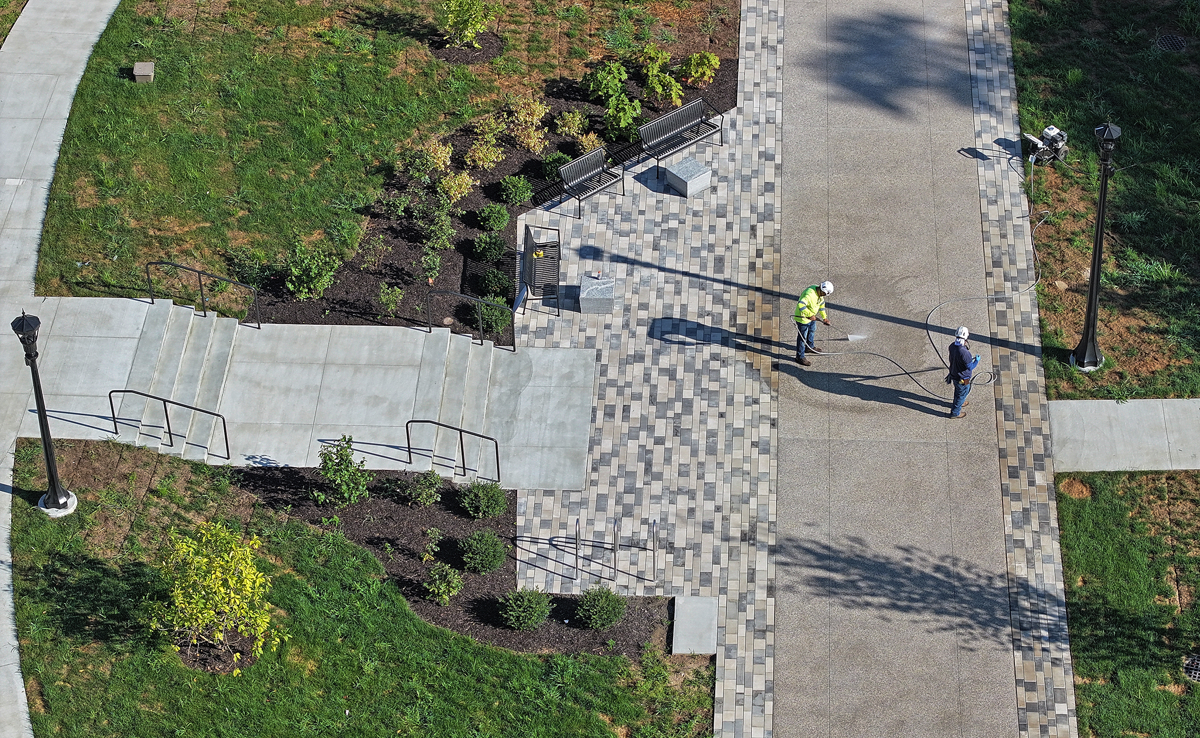 An aerial view of workers power washing a newly built pedestrian walkway on a college campus.