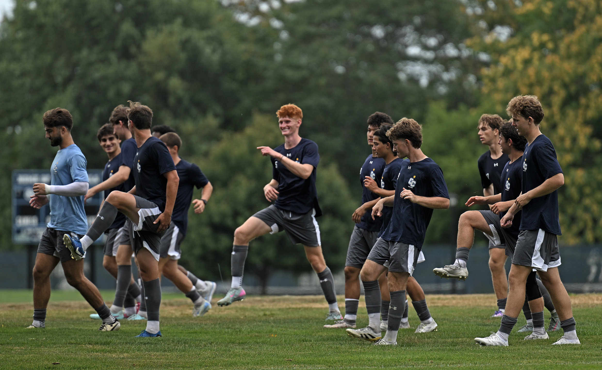 A men's college soccer team warms up on a field for practice.