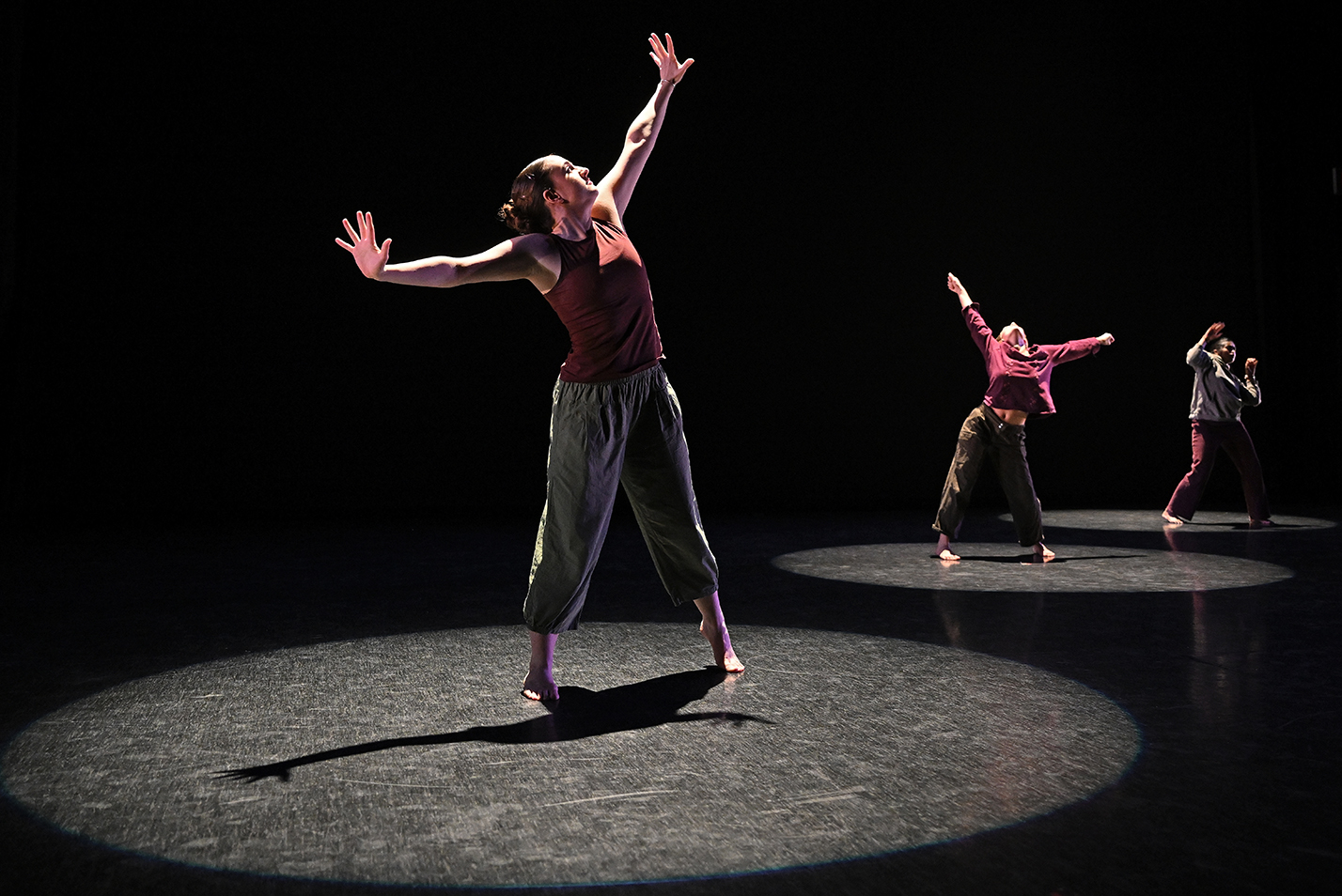 Dancers illuminated in pools of spotlight perform a modern dance piece.