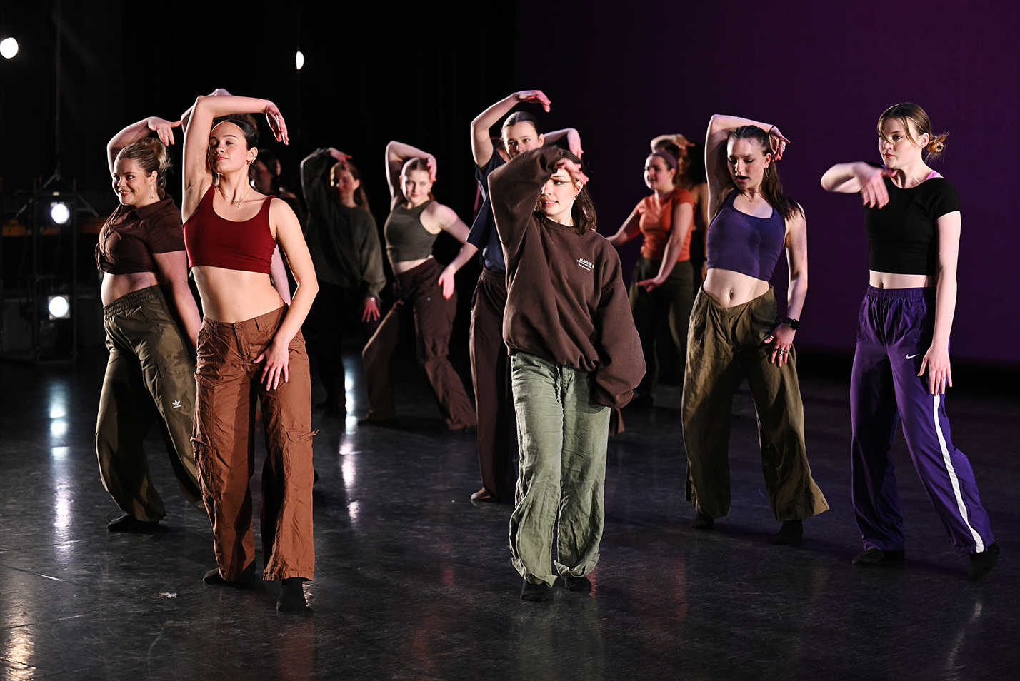 A large group of dance students wearing a variety of colorful outfits perform a modern dance piece.