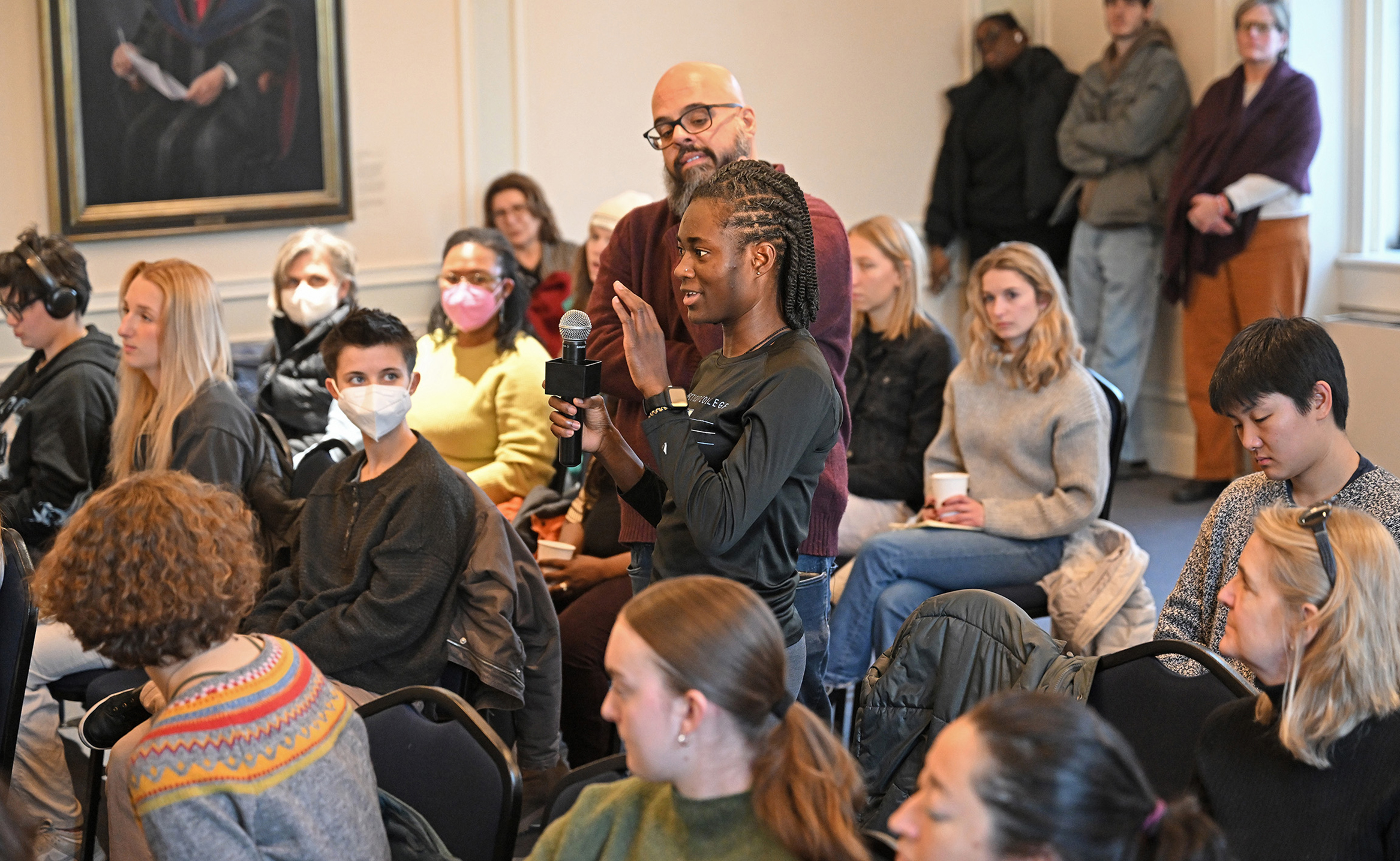 A man holds a microphone as a female student asks a question during a forum on housing justice