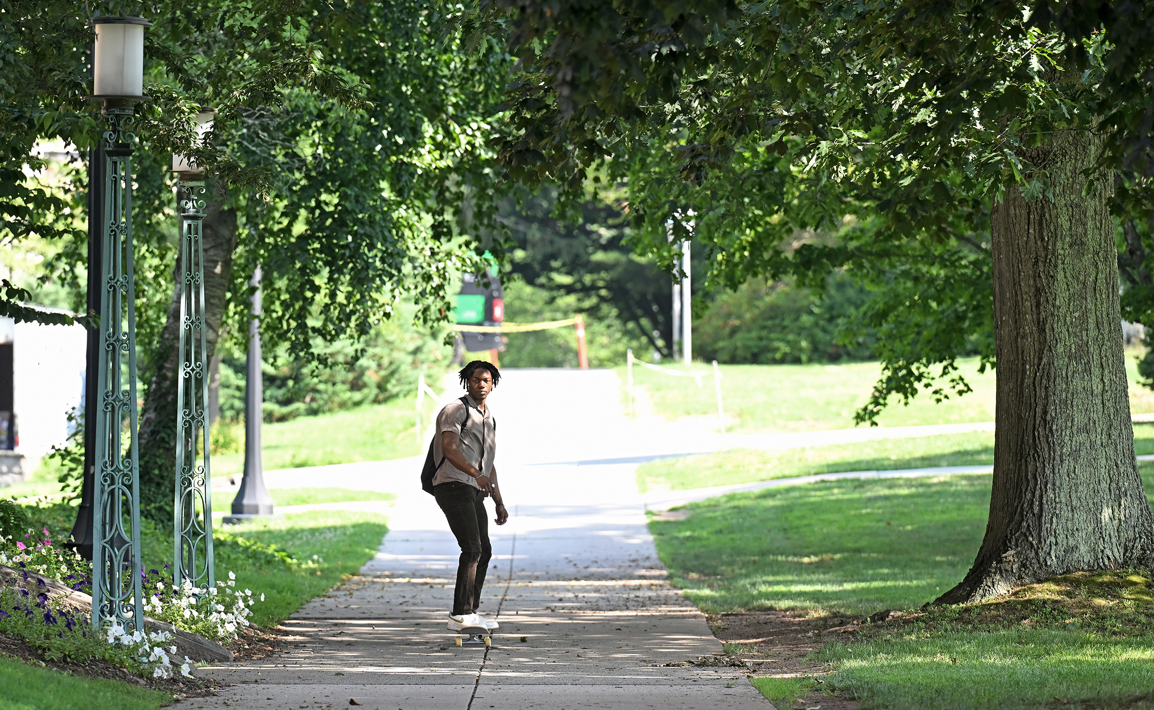 A college student rides a skateboard along a campus path.