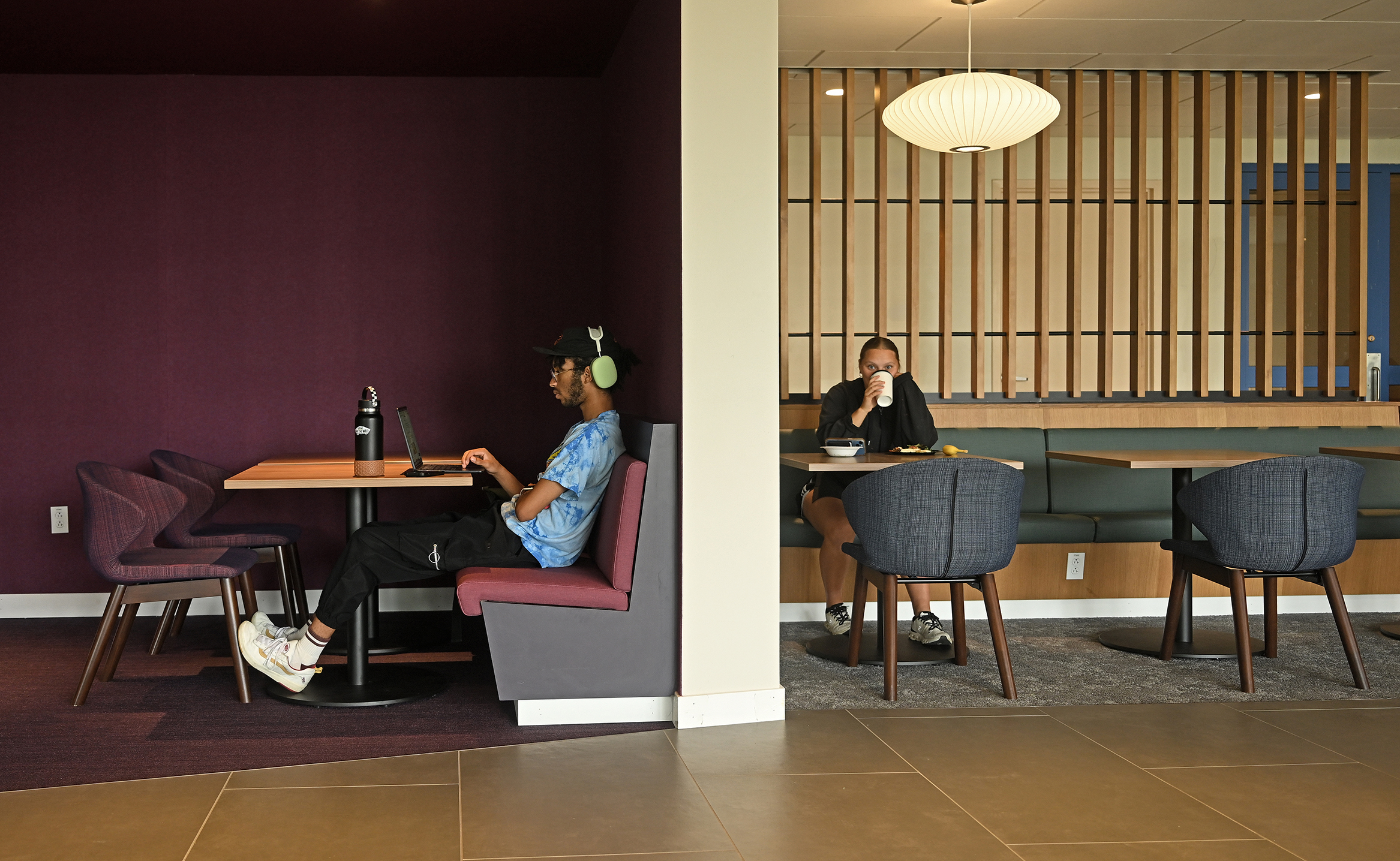 Two college students sit at separate seating areas studying and eating lunch.