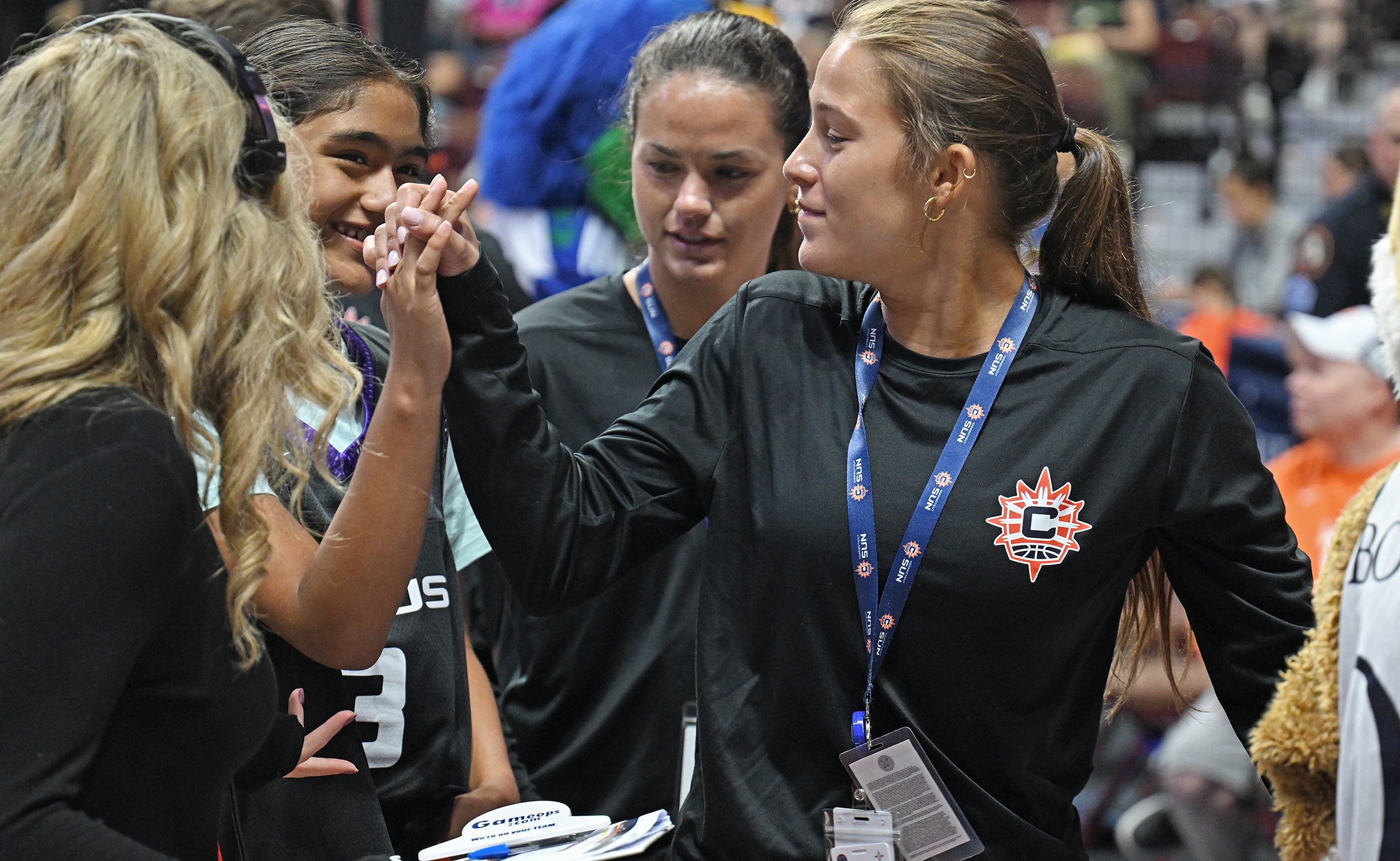 Two college students interact with children during a timeout activity at a professional basketball game.