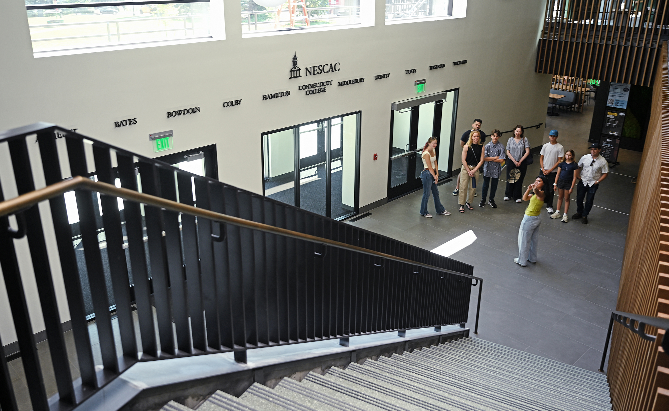 A college admissions tour stands at the bottom of a stairway in a student center foyer.