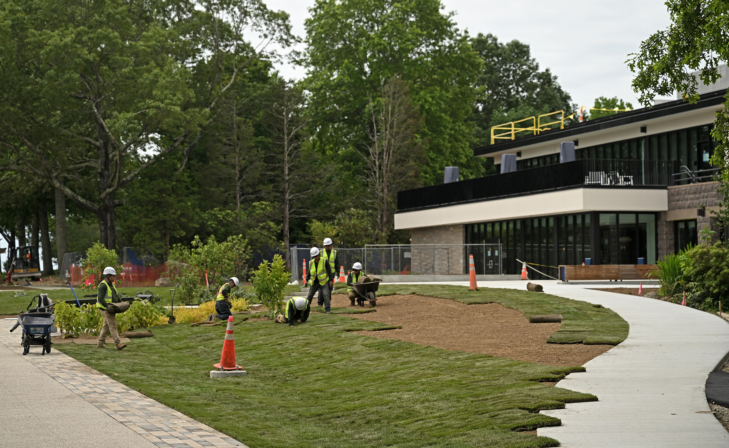 Landscapers plant grass and shrubs and trees between the pathways leading to a college student center.