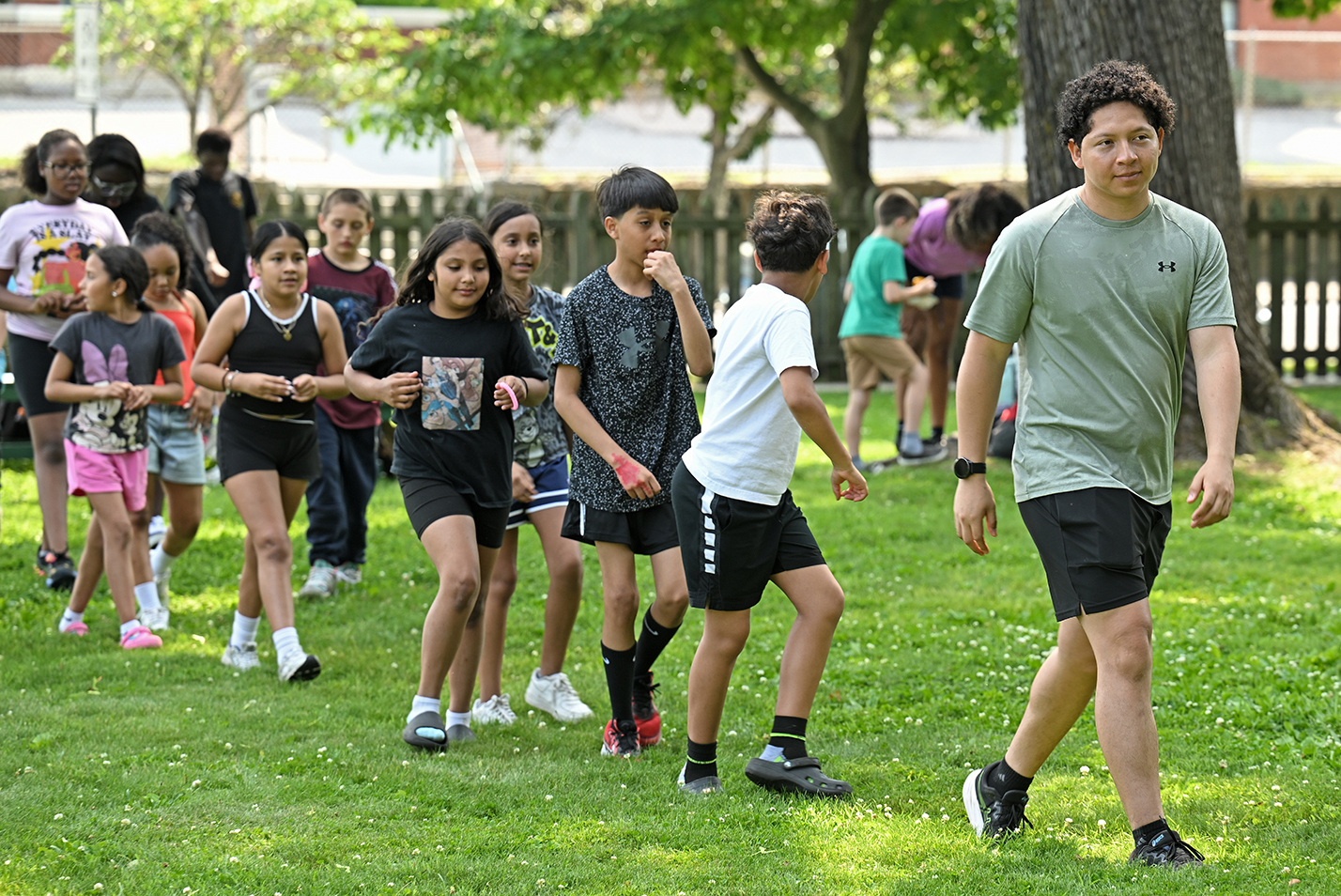 A college student leads a group of school-age children across a field during a summer camp internship.