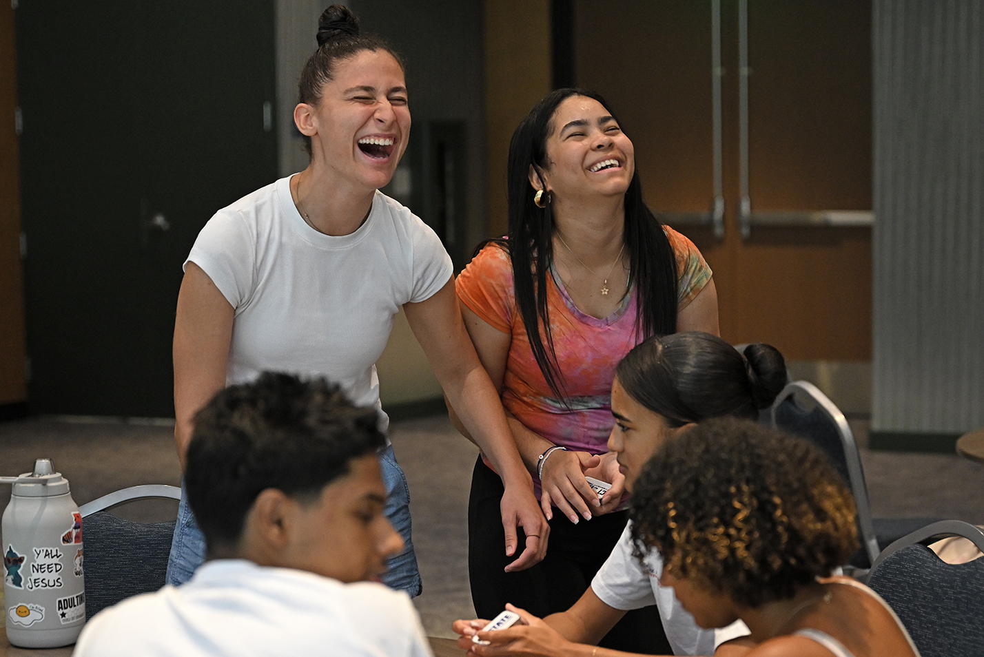 Two college students laugh while talking to high school students as part of a summer internship.