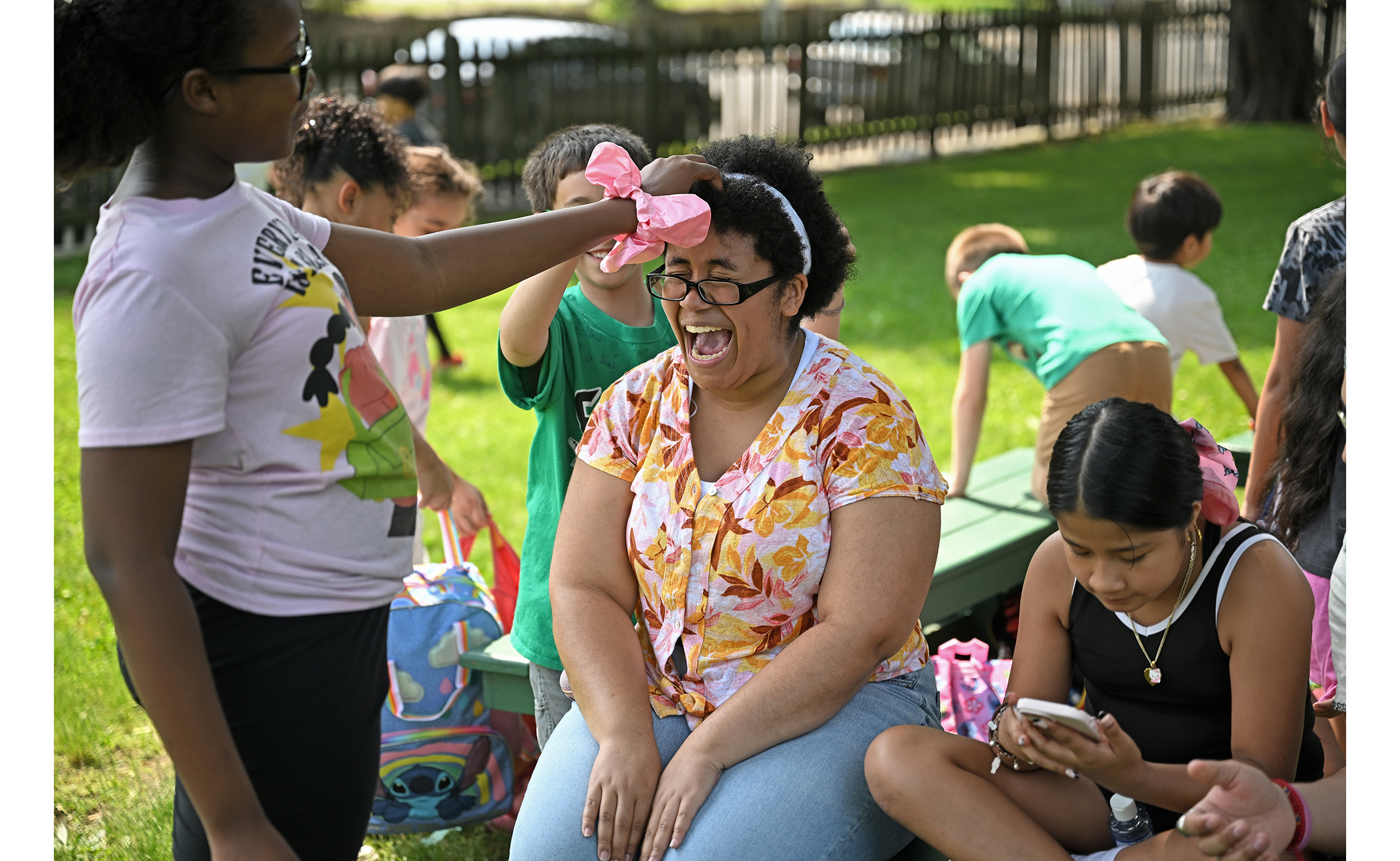 A student intern in a floral blouse laughs while working with children during an after-school program field day.