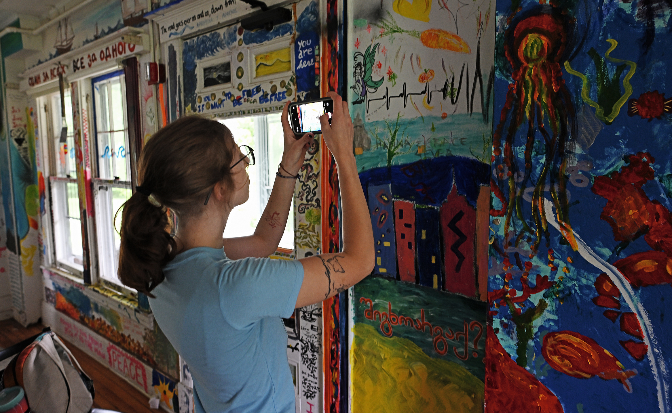 A student with a smart phone takes photos of elaborate murals painted on the walls of a college residence hall.
