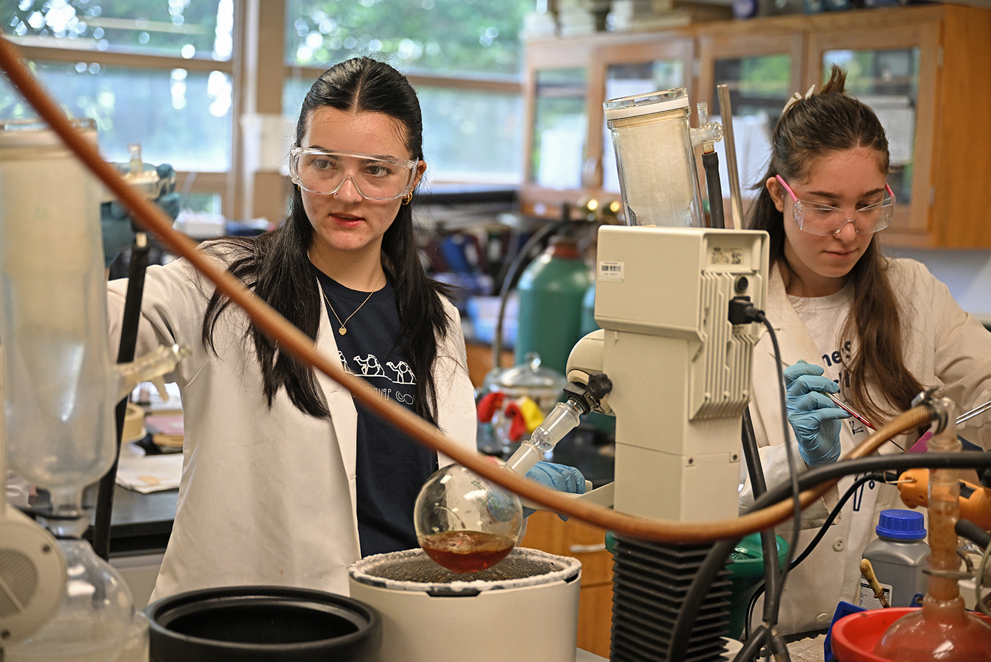Two student researchers in eye protection and lab coats work in a chemistry lab.