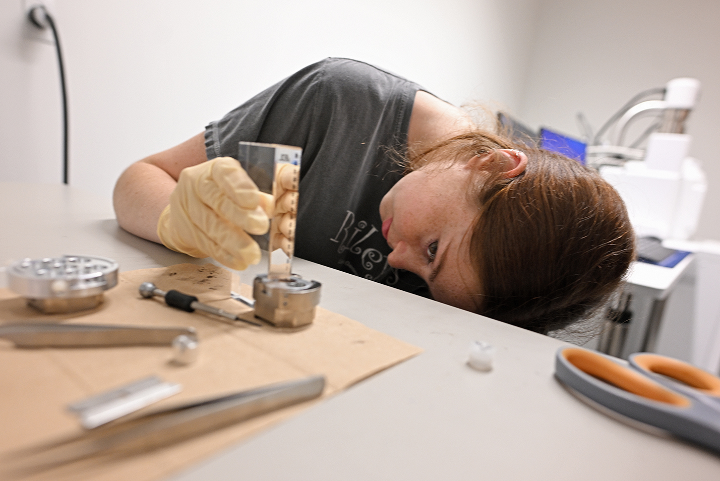A student researcher leans over to carefully check the measurement of a lab instrument.