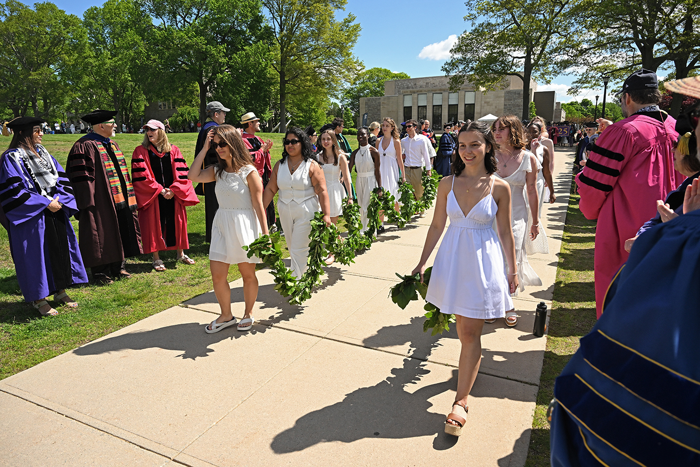 An honor escort dressed all in white and carrying a chain of greens processes down a sidewalk at the opening of commencement exercises.