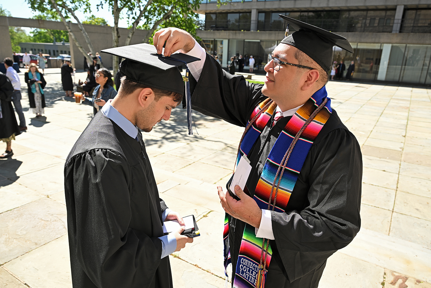 One graduate helps another to fasten the tassel on his mortarboard as they prepare for commencement exercises.