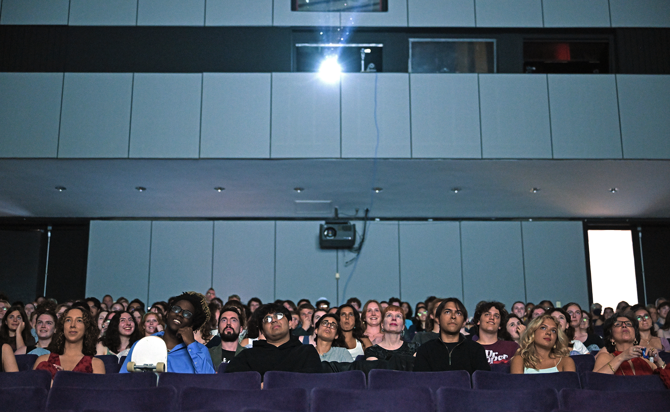 An audience watches a film exhibition in a darkened theater space.