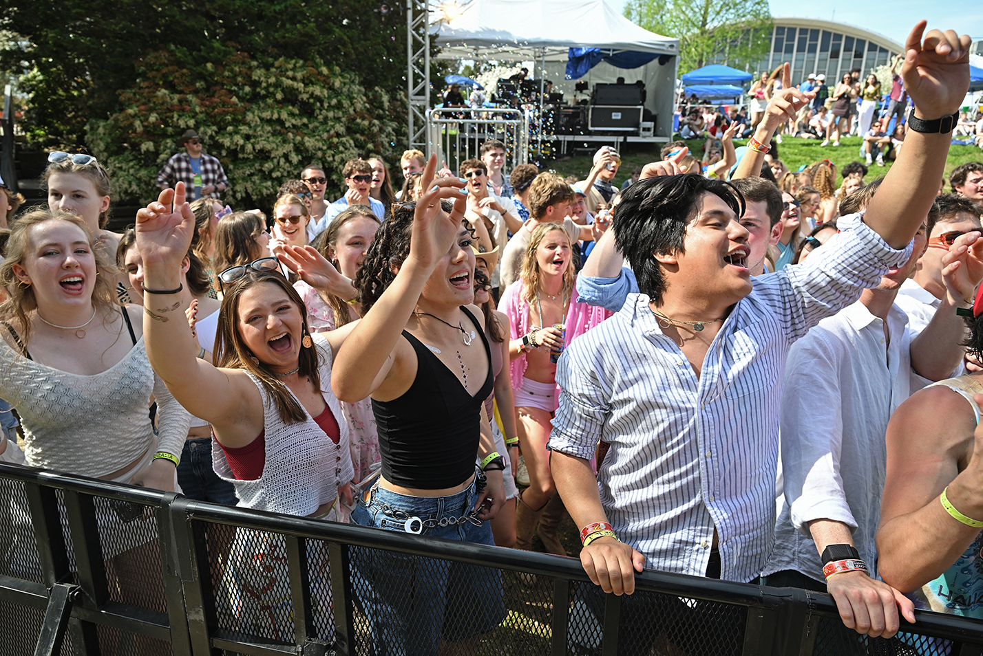 A crowd of students sing and dance at the barricade during an outdoor music festival.