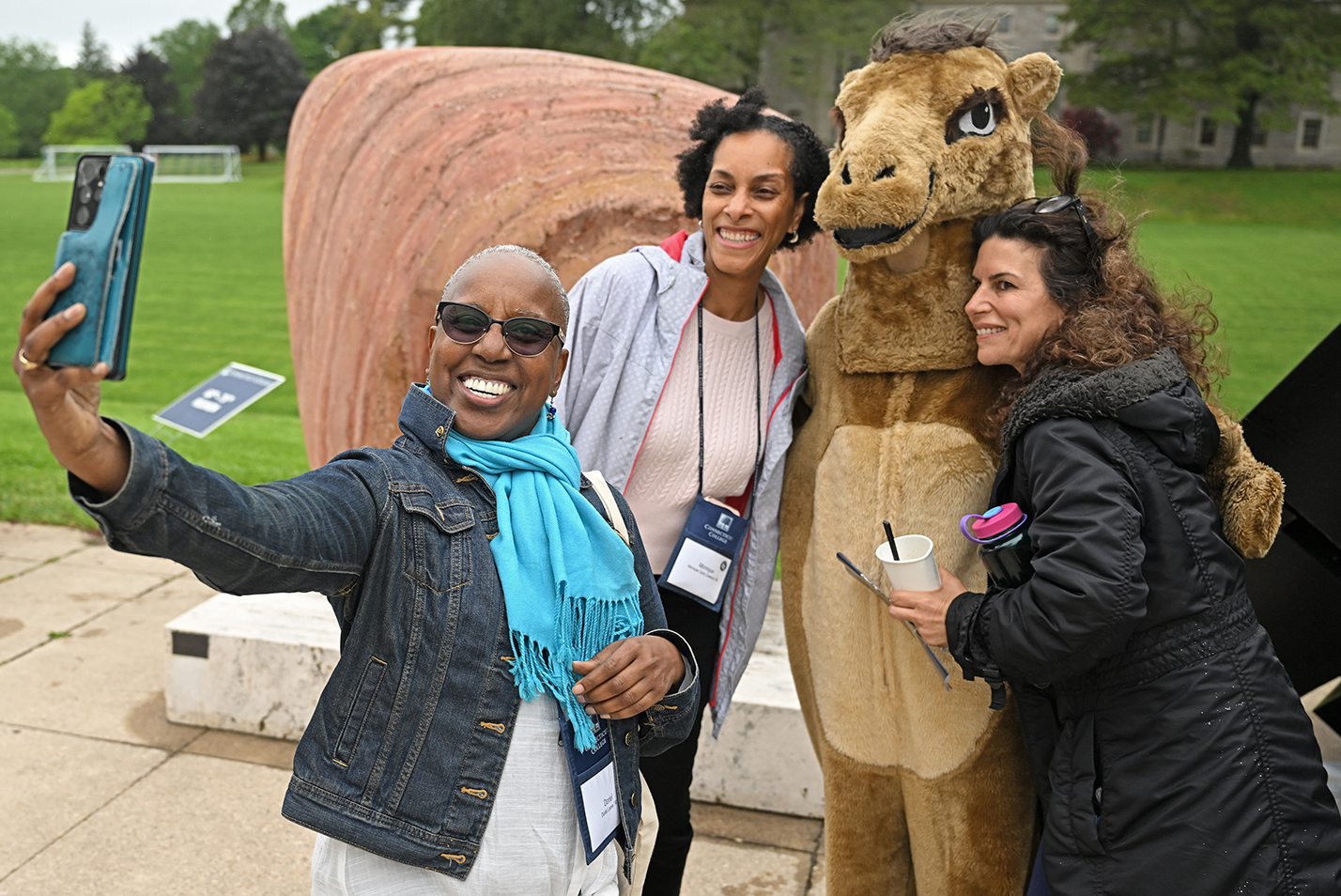 A group of college alumni take a photo together with the college camel mascot.