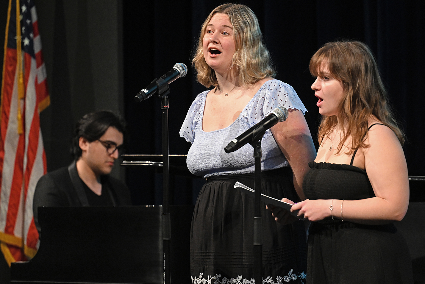 Two college students, accompanied by one on piano, sing the school's Alma Mater.