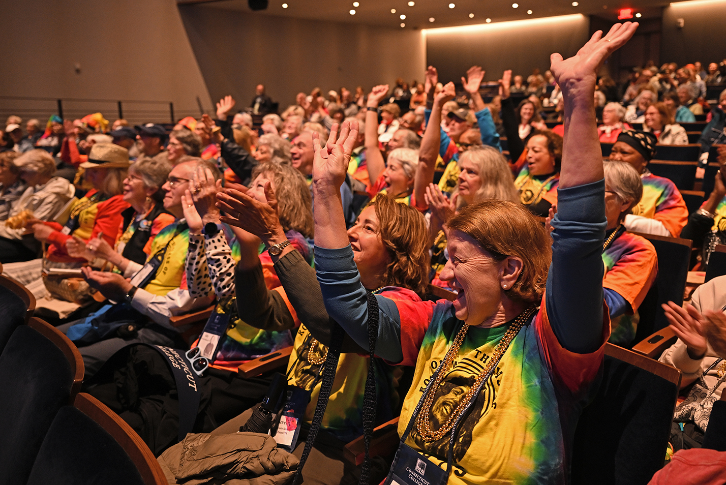 College alumni in rainbow colored shirts cheer a fundraising announcement during a reunion event.