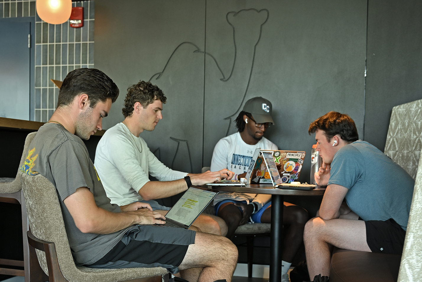 A group of male students gather around a table in a college pub space to study for finals.