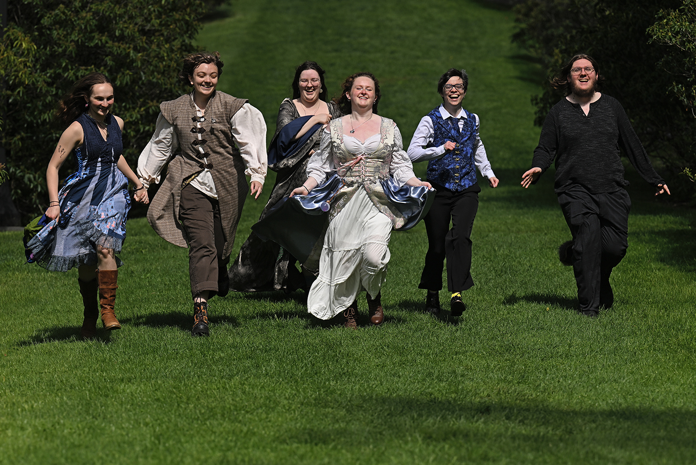 Costuming students run down a grassy hillside as part of a final presentation of their semester's projects.
