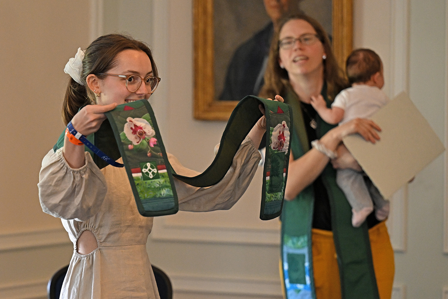 A student holds up the ends of an honors stoll embroidered with orchid flowers.